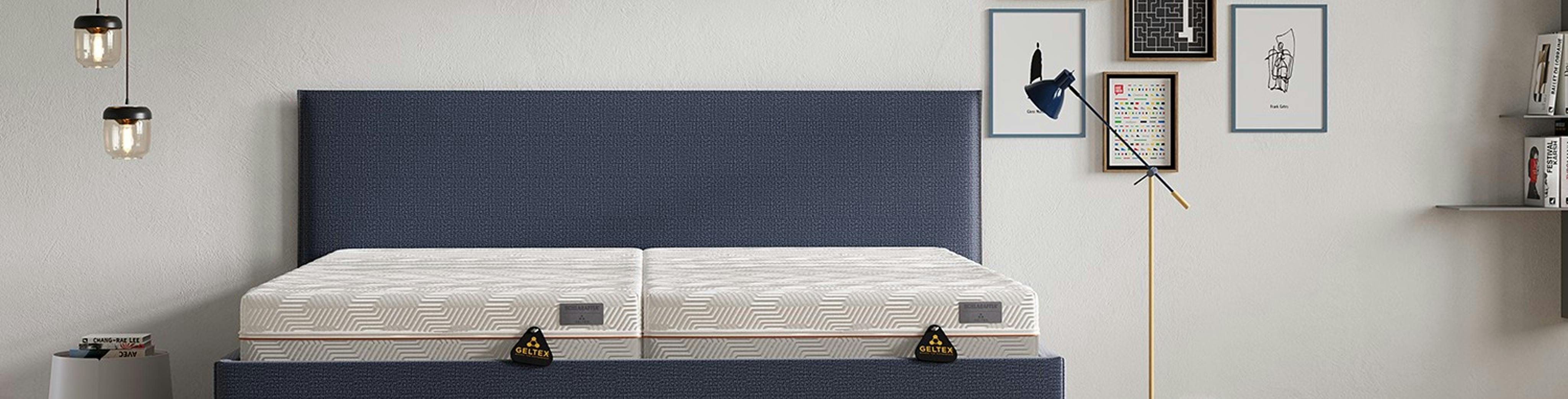 Schlafzimmer mit Pendellampen, Wandbildern und blaugrauem Polsterbett mit zwei Gelmatratzen