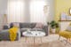 Helles Wohnzimmer mit hellgrauem Sofa, weißem Couchtisch und einer Stehlampe im Skandi-Stil, einem gelben Skandi-Sessel, einer Pendelleuchte aus Muscheln, einem weißen Sideboard und schönen Textilien.