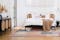 Camera da letto in stile rétro con letto davanti a una tenda bianca, poltrona e madia nere con inserti in paglia di Vienna, su tappeto moderno con motivo a quadri color pastello 