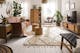 Wohnzimmer im Boho-Style mit einem Ledersofa, Holzmöbeln mit Wiener Geflecht, Rattan, vielen Pflanzen, Textilien und Deko aus Messing