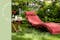 Ligstoel van hout met rood kussen (alternatief met wit hoofdkussen) in een groene tuin