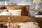 Slaapkamer in de boho-stijl met palmenbehang, meubels van het home24-merk kollected, bruin en wit textiel, een gebreide poef, vloerkleed, rotanlamp, zwarte spiegel en zwarte vazen.