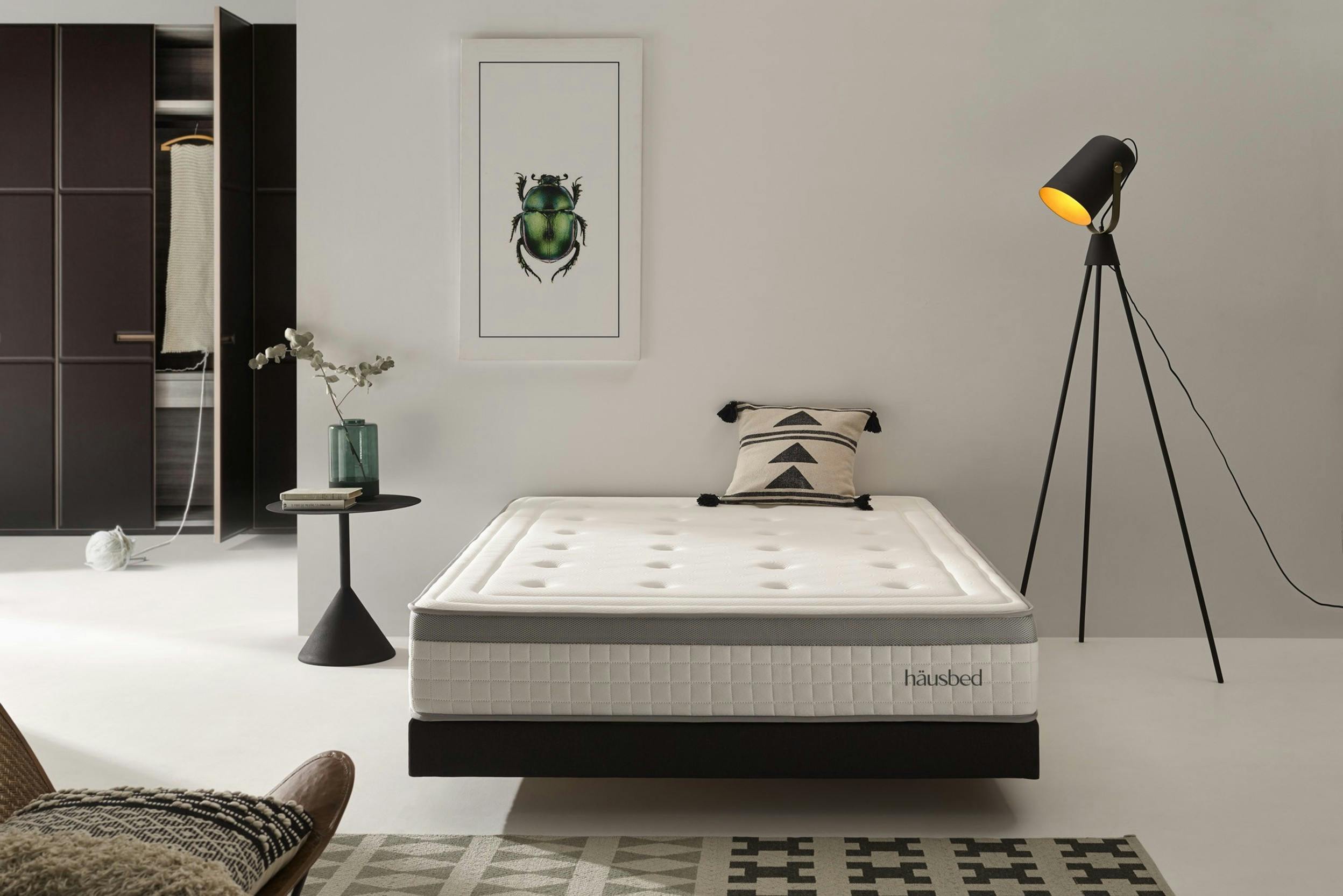 Schlafzimmer mit schwarzem Kleiderschrank, einer Tripod-Stehlampe und einem Bett mit Matratze