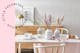Heller Holztisch mit drei Trockenblumensträußen in großen Vasen arrangiert; daneben ein Kranz aus beigen und rosanen Ziergräsern und Trockenblumen auf einem Sideboard dekoriert.