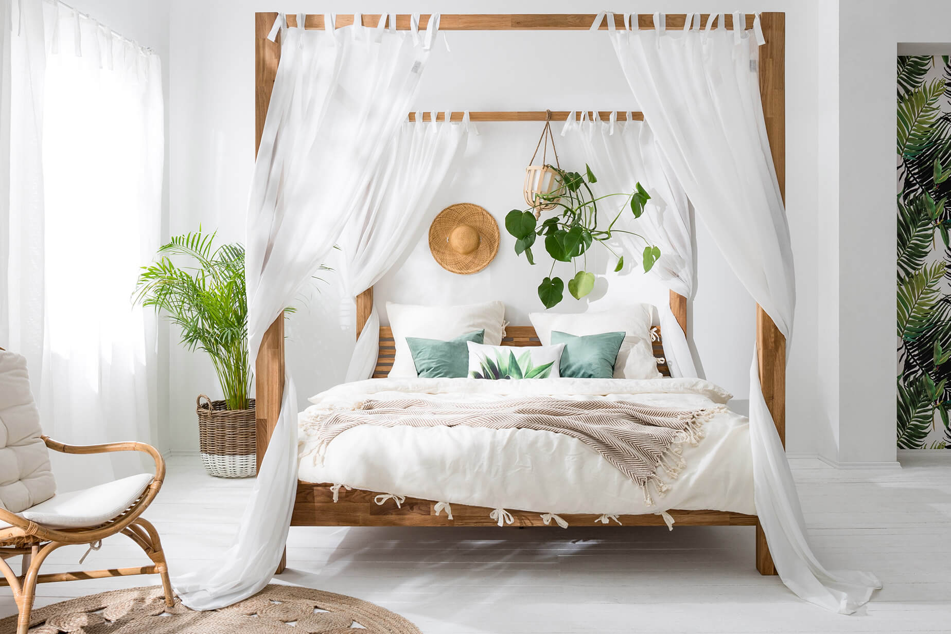 Schlafzimmer mit Himmelbett, weißer Bettwäsche, floralen Motiven und Rattansessel
