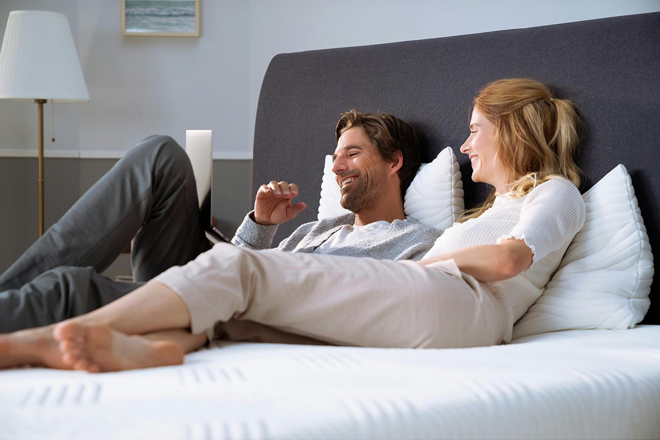 Lachendes Paar auf einer unbedeckten Matratze auf einem gepolsterten Bett mit einem großen Kopfteil