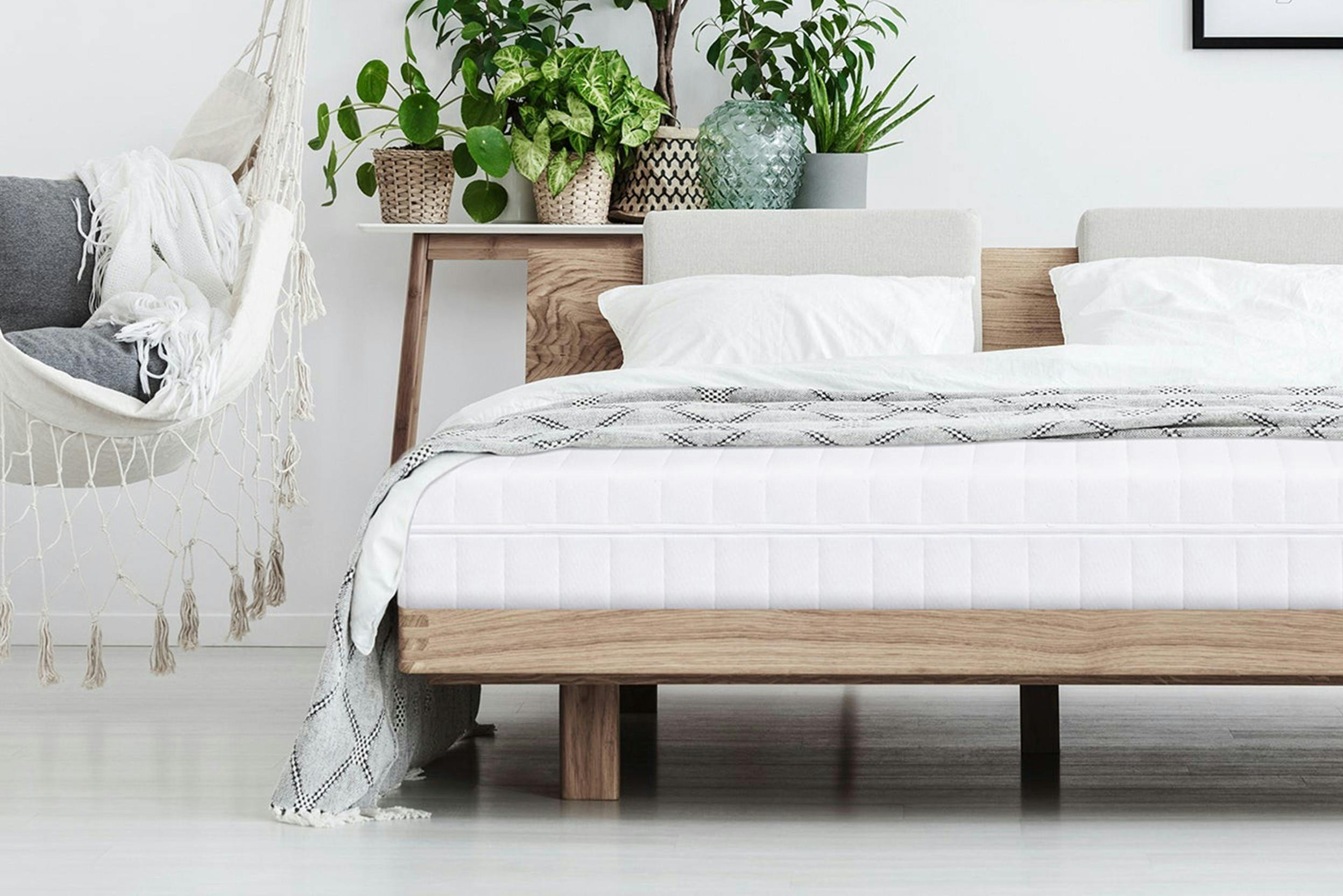 Schlafzimmer mit Grünpflanzen, Hängesessel und Holzbett mit Matratze