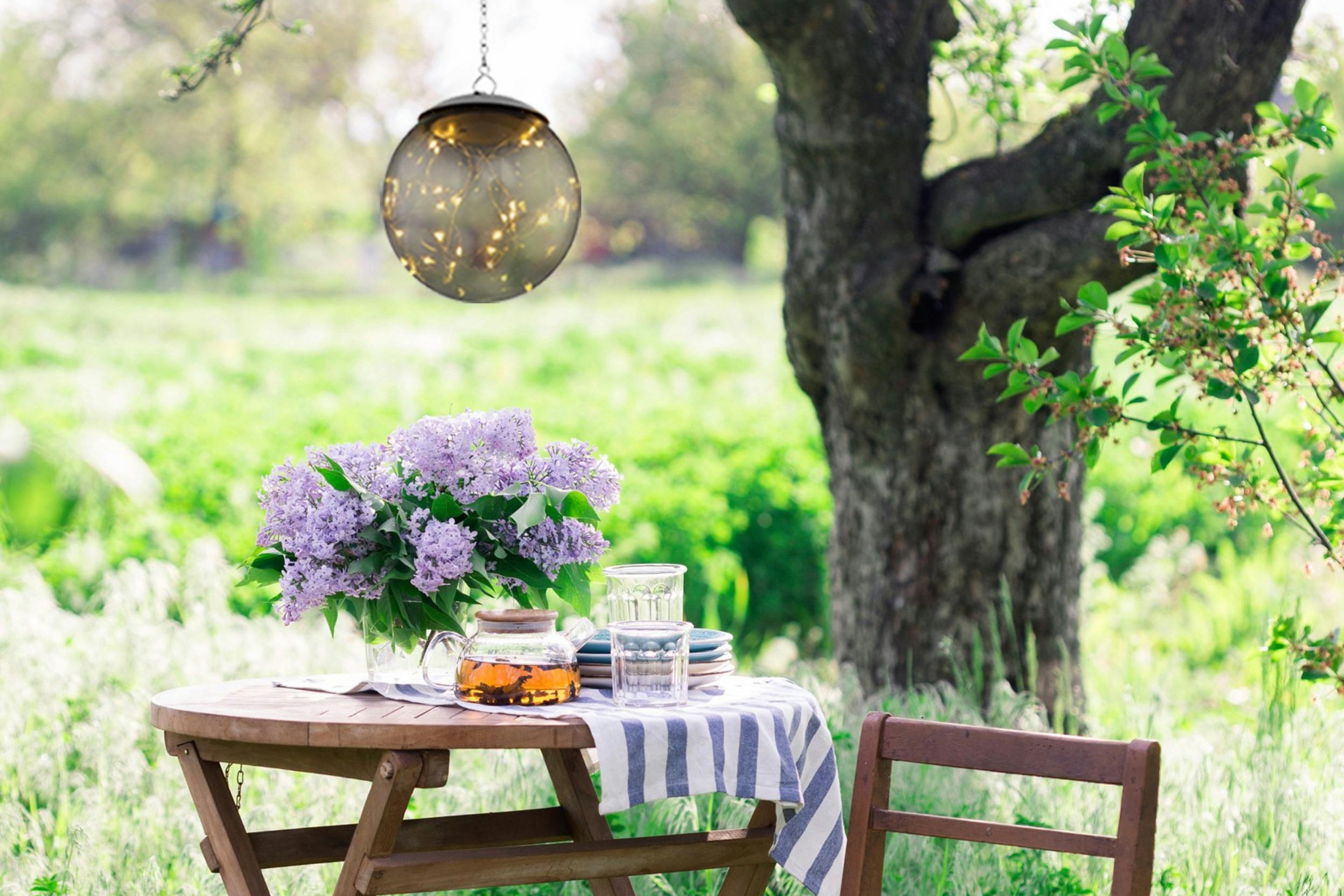 Rustikaler Gartentisch neben einem alten Baum mit darüber hängender LED-Pendelleuchte