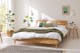 Bettgestell aus Holz in hellem Schlafzimmer mit Grünpflanzen