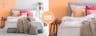 Lit boxspring gris clair Avellino par Mørteens, avec coussins et peinture murale  couleur Peach Fuzz, la couleur Pantone de l'année 2024, ainsi que divers textiles et plantes, une étagère échelle, une table d'appoint et un plafonnier cuivré.