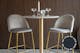 Sedie grigio chiaro e tavolo da bar dalla struttura color oro con due bicchieri di cristallo e due portacandele di vetro sul piano in marmo