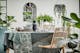 Sala da pranzo con tavolo di legno e sedie in rattan, piante, piatti neri e grigi e bicchieri di BUTLERS.