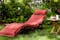 Houten ligstoel met rode bekleding in het midden van een groene tuin