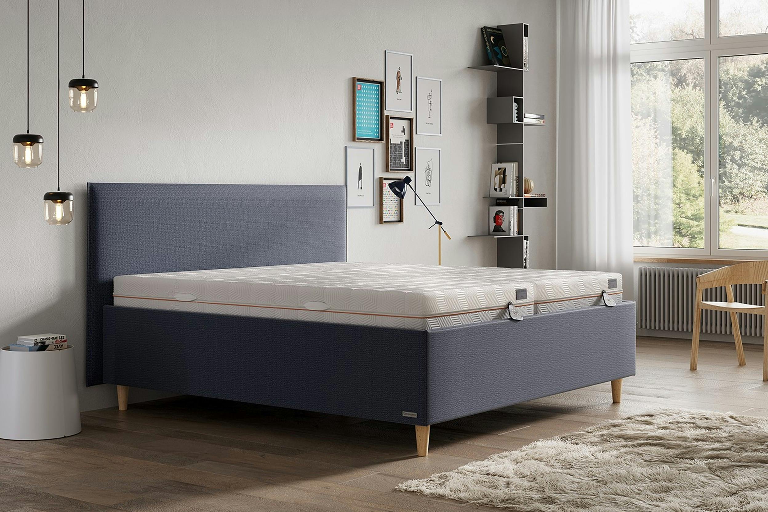 Schlafzimmer mit Pendellampen, Wandbildern und blaugrauem Polsterbett mit zwei Gelmatratzen