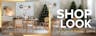 Sala da pranzo con mobili della collezione Studio Copenhagen: tavolo da pranzo in legno chiaro con sedie in rattan, una madia, una poltrona grigia e lampade a sospensione di vetro; albero di Natale decorato, decorazioni natalizie e vaso bianco e nero, piatti e bicchieri neri.