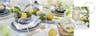 Table dressée avec du linge de table blanc, de la vaisselle bleue, des couverts dorés et de beaux citrons jaunes avec leurs feuilles pour la décoration, le tout accompagné de Limoncello Spritz dans des verres à pied BUTLERS.