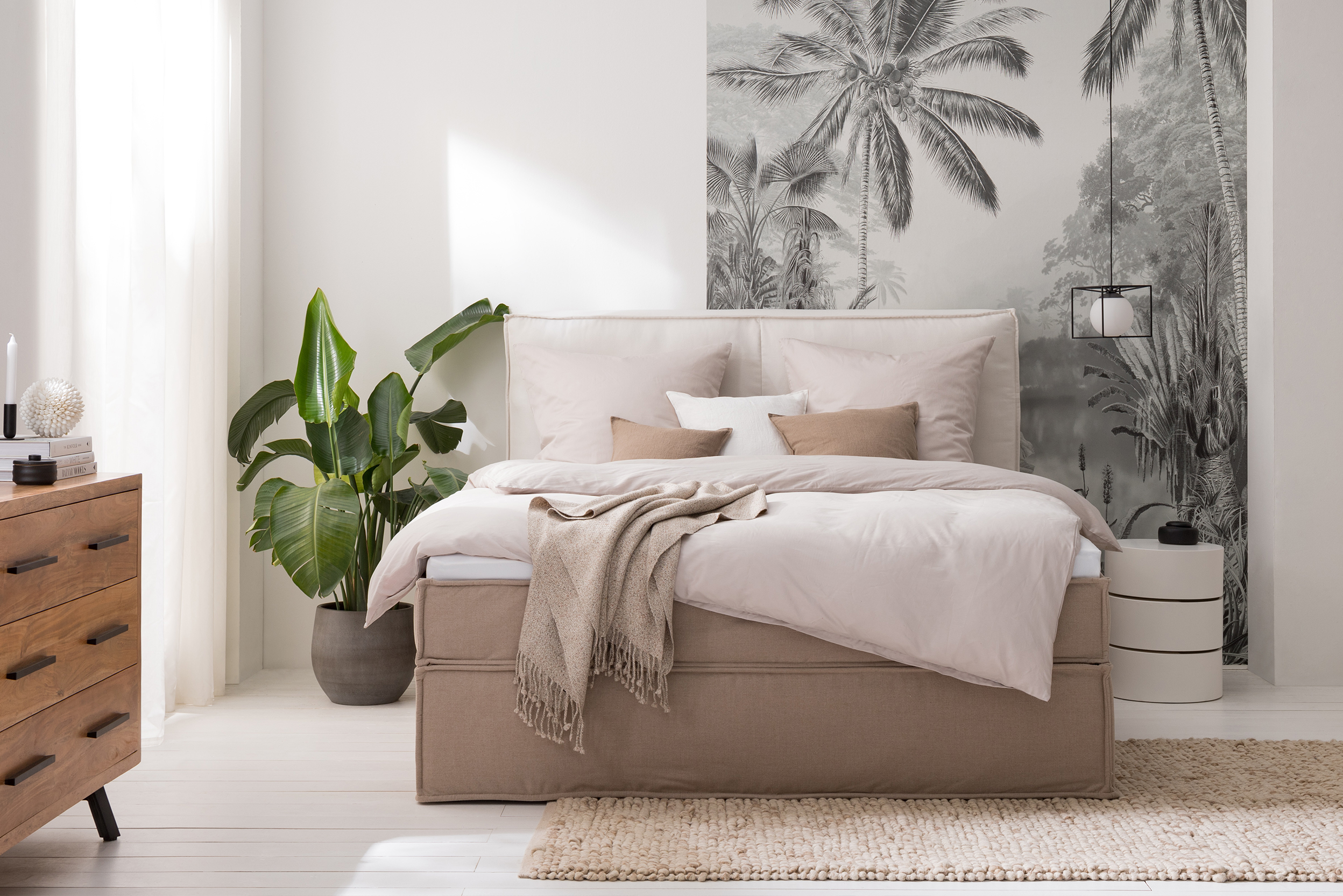 Schlafzimmer in Cremefarben mit einem Boxspringbett in Beige und heller Bettwäsche, dazu eine Kommode und Pendelleuchte im Industrial-Stil.