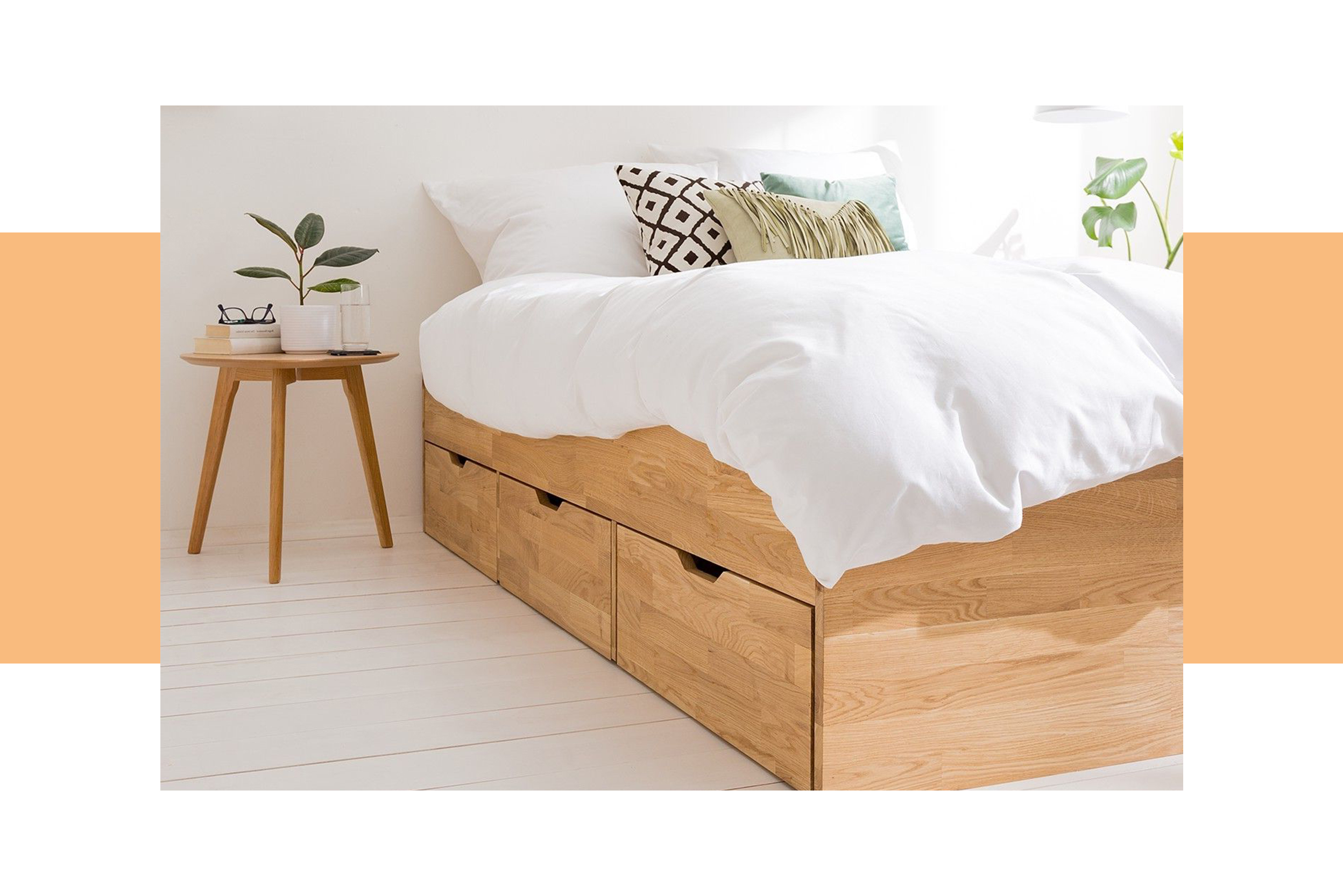 Stauraumbett aus hellem Holz mit 3 Schubkästen, weißer Bettwäsche und weißen Pendellampen über dem filigranen Nachttisch.