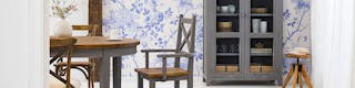 Meubles de salle à manger gris de style maison de campagne devant du papier peint fleuri bleu et banc.