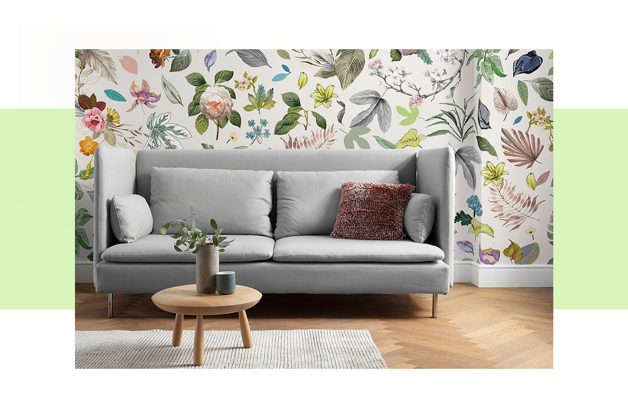 Graues Sofa vor einer Wand mit Blumenprinttapete, dazu ein runder Couchtisch aus Holz, Tischdeko sowie ein grauer Teppich; daneben schöne Blumenvasen in Grüntönen.