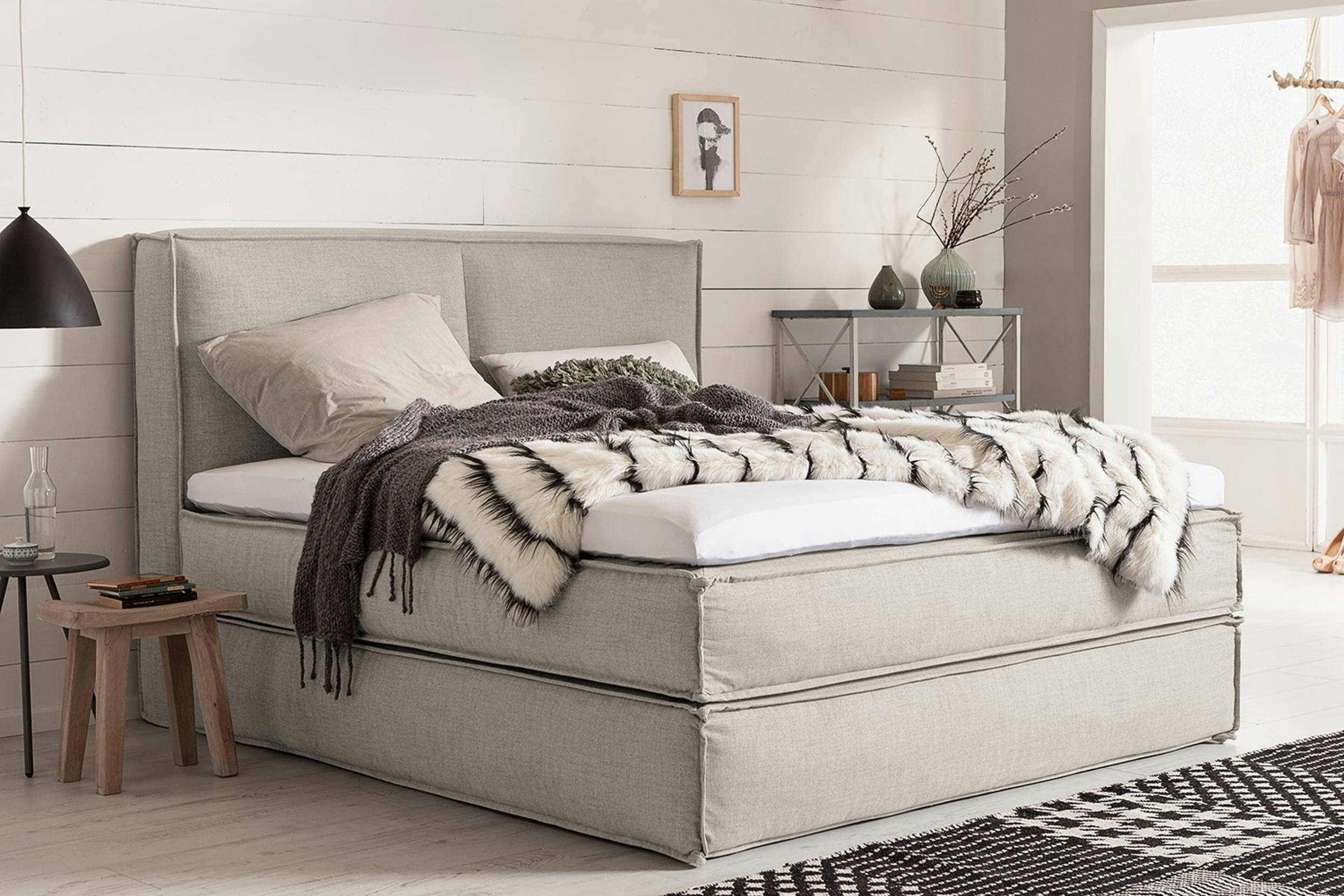 Lit boxspring de couleur beige clair, dans une chambre aux mêmes tons, avec jeté de lit et déco minimaliste.