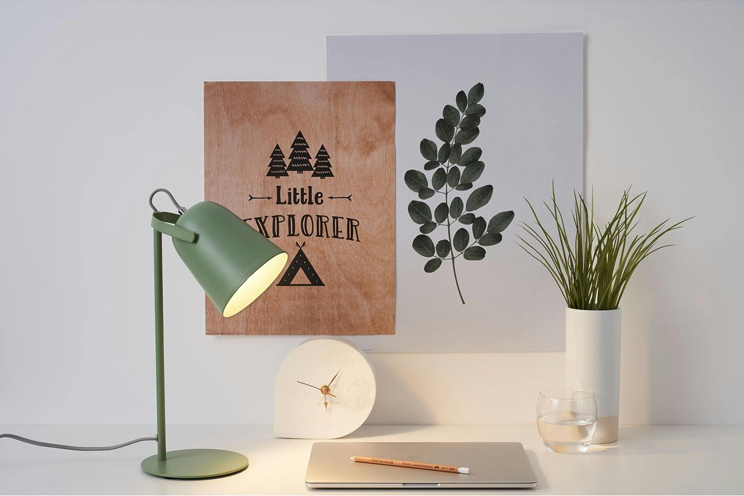 Grüne Schreibtischlampe auf weißem Schreibtisch mit Pflanze und Bildern im Hintergrund