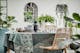 Eetkamer met houten tafel en stoelen van rotan omgeven door veel groene planten, plus schalen, serviesgoed in zwart en grijs en stijlvolle glazen van het merk BUTLERS.