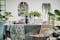 Salle à manger avec table en bois et chaises en rotin, entourée de nombreuses plantes vertes, avec des bols, de la vaisselle en noir et gris et des verres élégants BUTLERS.