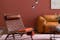 Salon avec fauteuil en cuir tressé, canapé en cuir cognac, table basse noire en verre et métal, lampadaire noir, tapis rose ; le tout devant un mur tirant sur le orange.