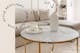 Woonkamer met beige interieur met als middelpunt een salontafel met wit marmeren tafelblad en gouden meubelpoten.