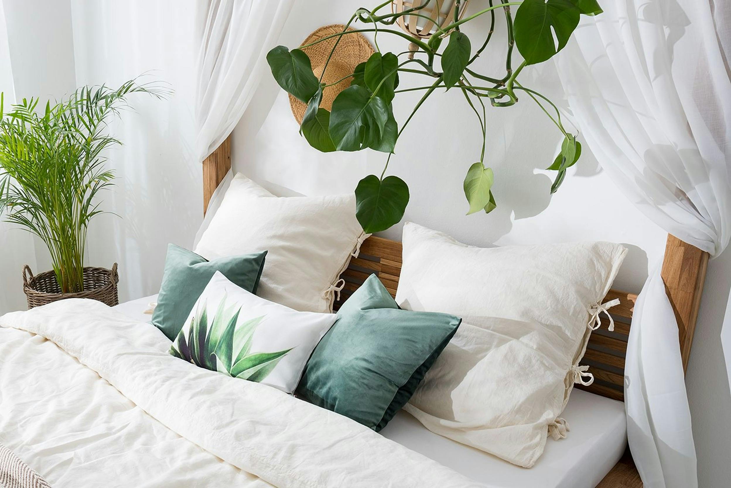 Opgemaakt bed met wit beddengoed en groene kussens, plafondplanten