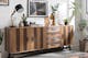 Sideboard der Serie Tamati by kollected im rustikalen Fabrikstil mit zweifarbigem Holz, darauf diverse Deko-Gegenstände wie Vasen und eine Industrial-Lampe, daneben eine Palme im Rattankorb.