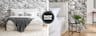 Letto boxspring KINX bianco con lenzuola bianche di fronte a una parete effetto marmo. Due lampade a sospensione bianche e nere, un tappeto bianco e soffice e mobili in stile rétro in legno color nero con inserti in paglia di Vienna.