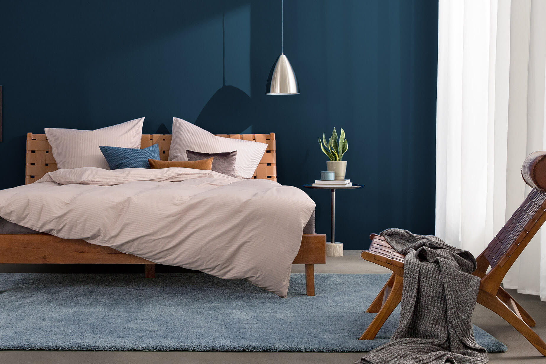 Schlafzimmer in dunkelblauen Nuancen mit Massivholzbett und Stuhl in Flechtoptik