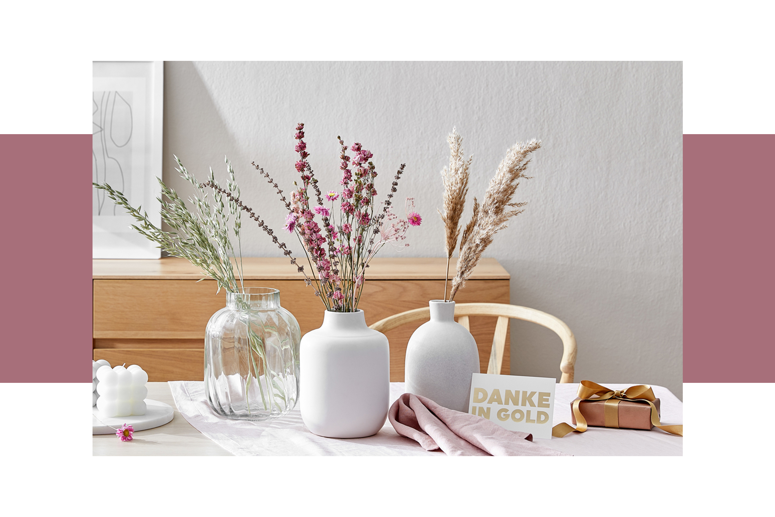 Heller Holztisch mit drei Trockenblumensträußen in großen Vasen arrangiert