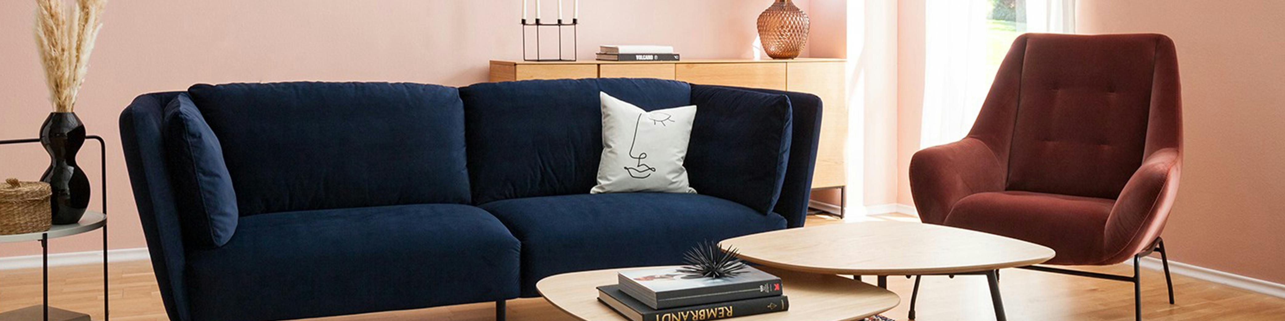 Blaues Samtsofa im Wohnzimmer mit Couchtisch aus Holz und gepolstertem Sessel kombiniert
