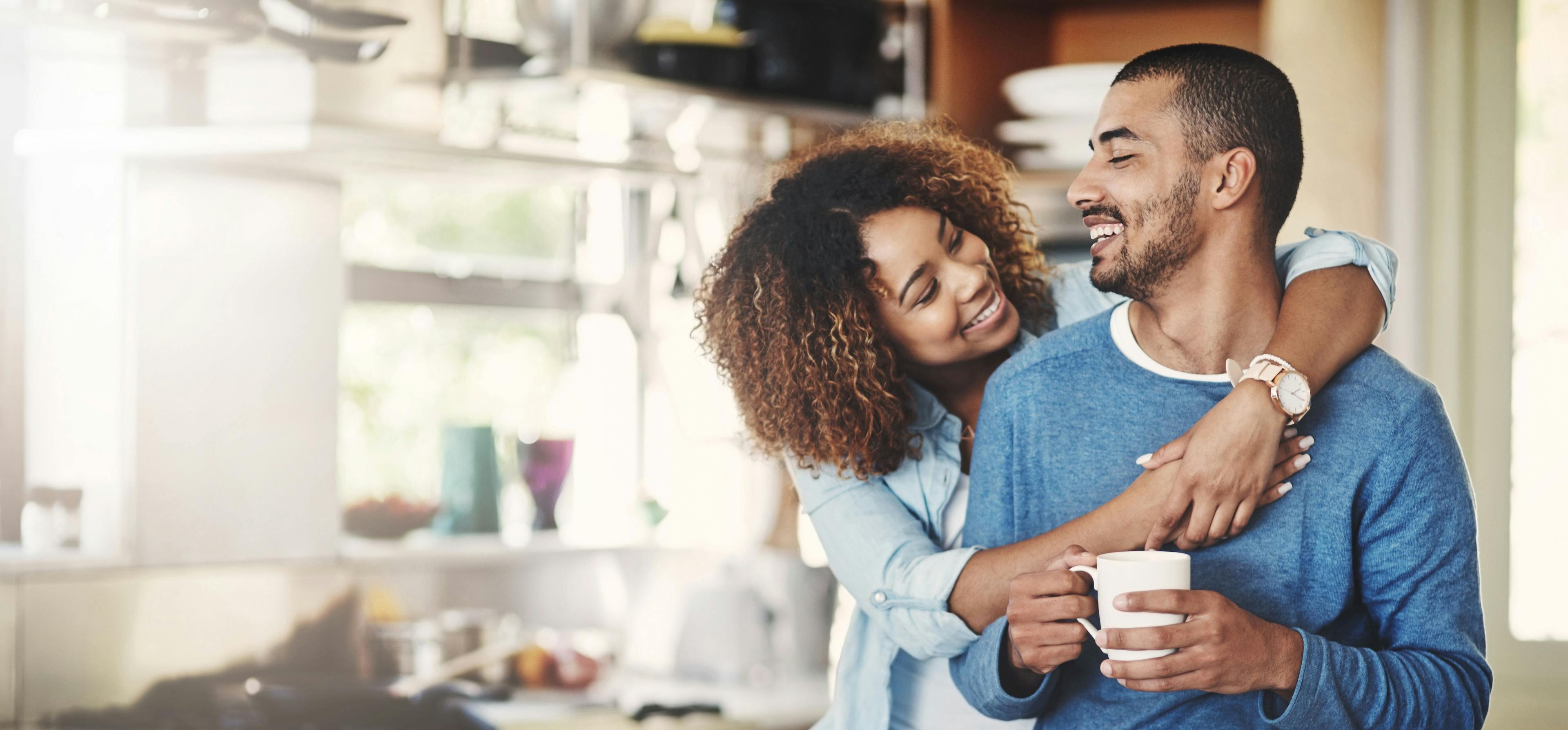 Woman embraces man from behind while he looks back into her eyes