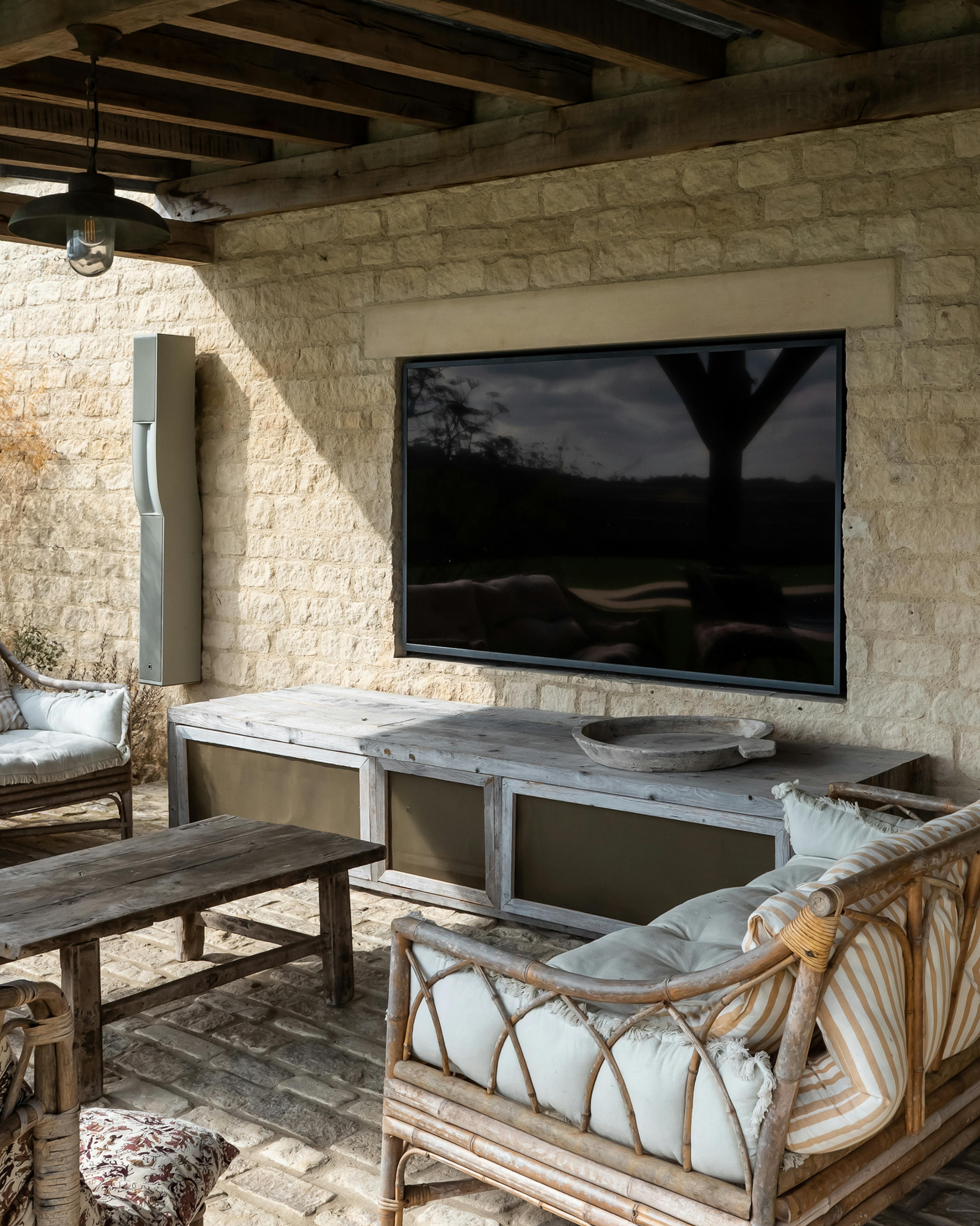 Weatherproof television recessed into a Cotswold stone wall above a garden sofa