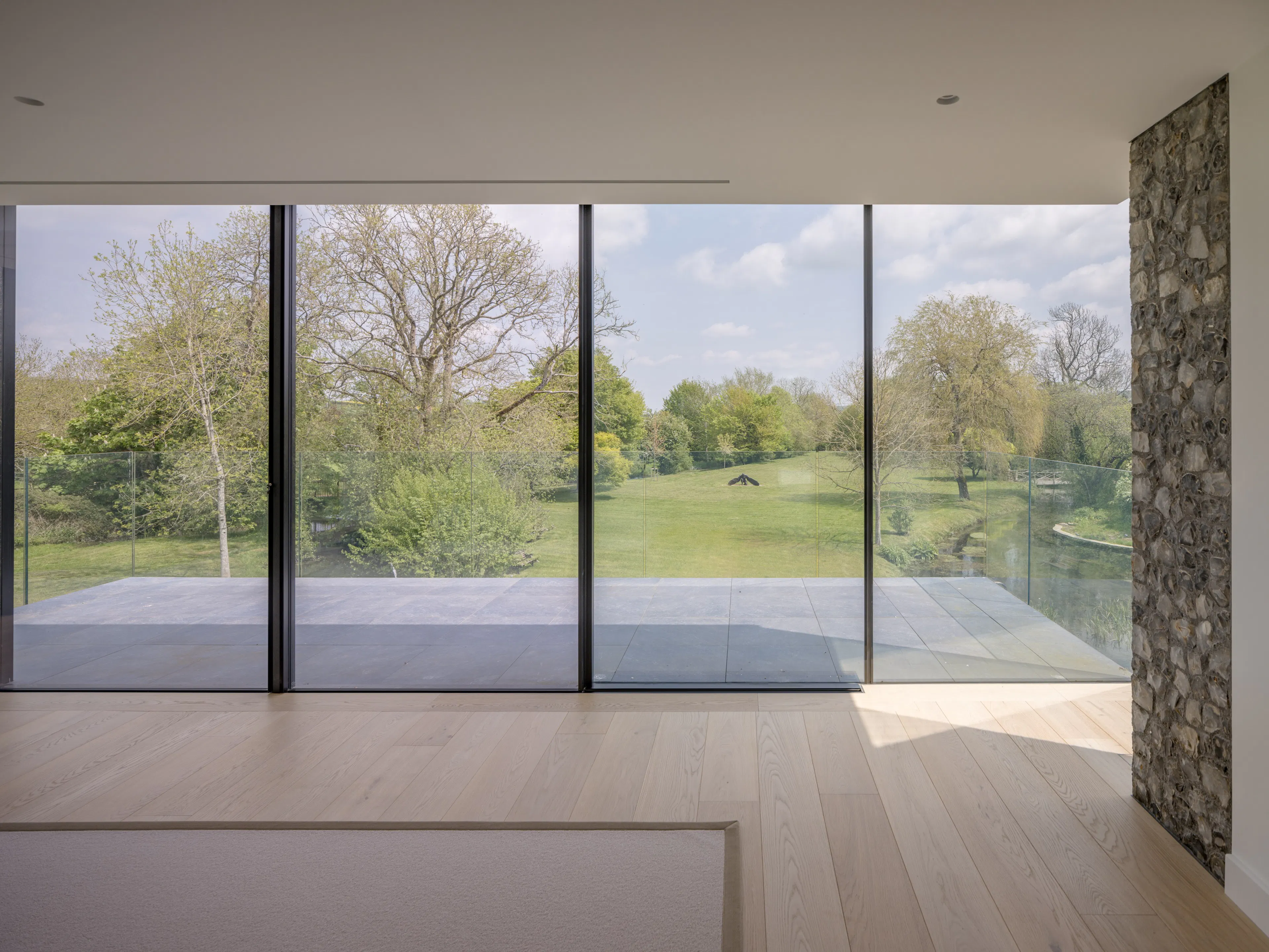 Living room in the glass wing with floor-to-ceiling glazing, a flint wall and views over the water meadows
