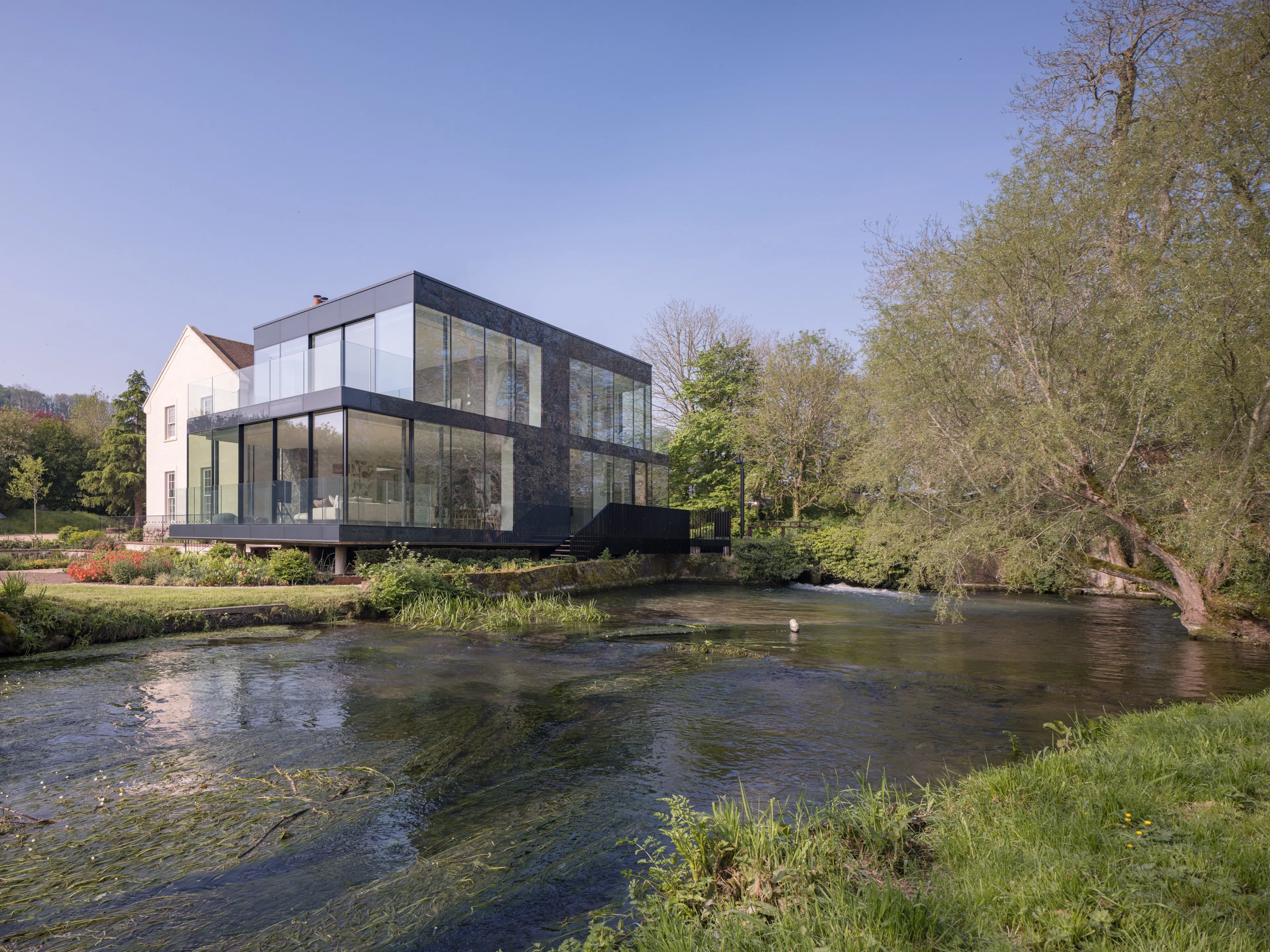 The old mill house and its new glass wing seen across the river on a spring day
