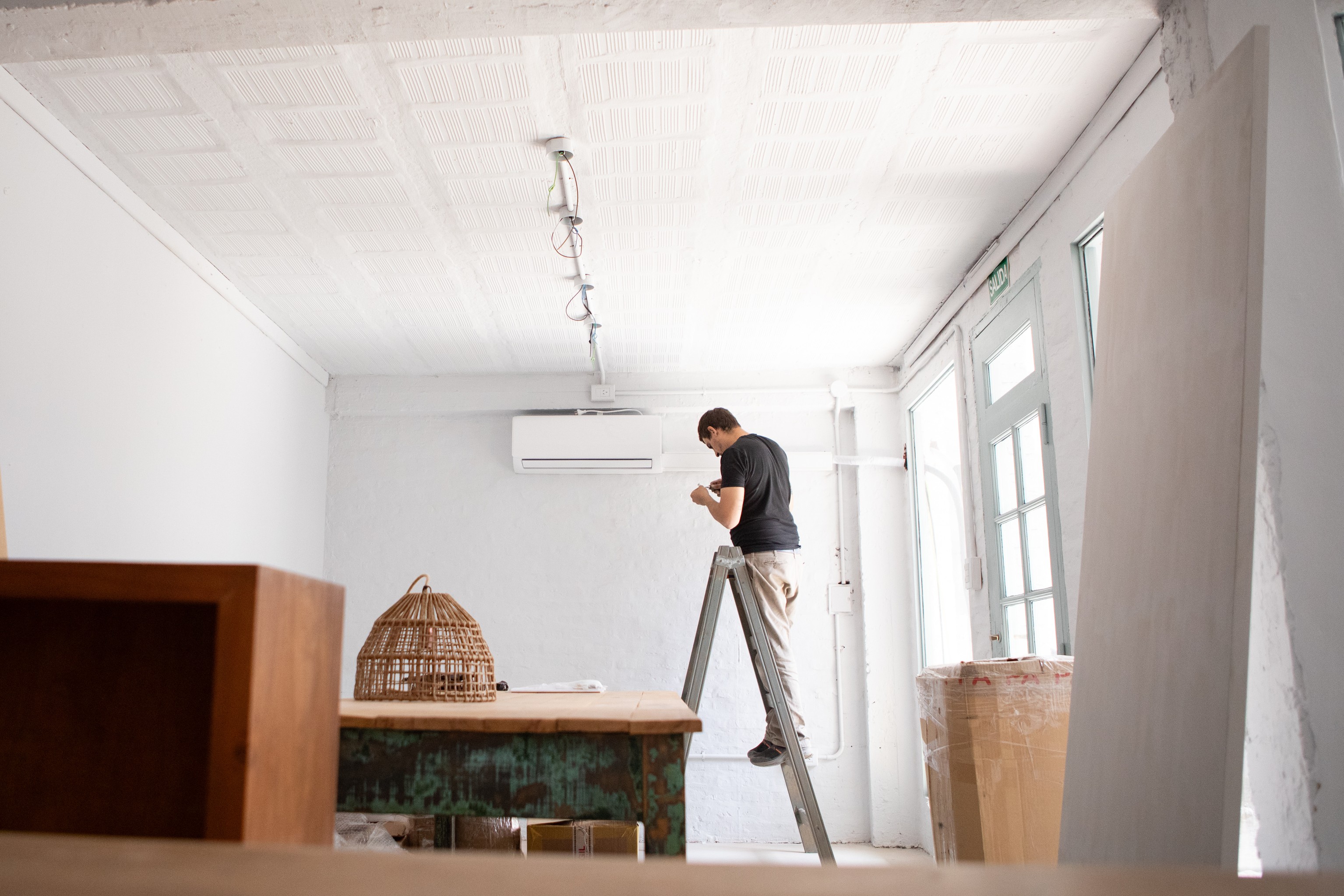 Homme sur une échelle installant l'unité intérieure de sa climatisation. Installer soi-même sa clim : grosse erreur ou bonne idée ? 