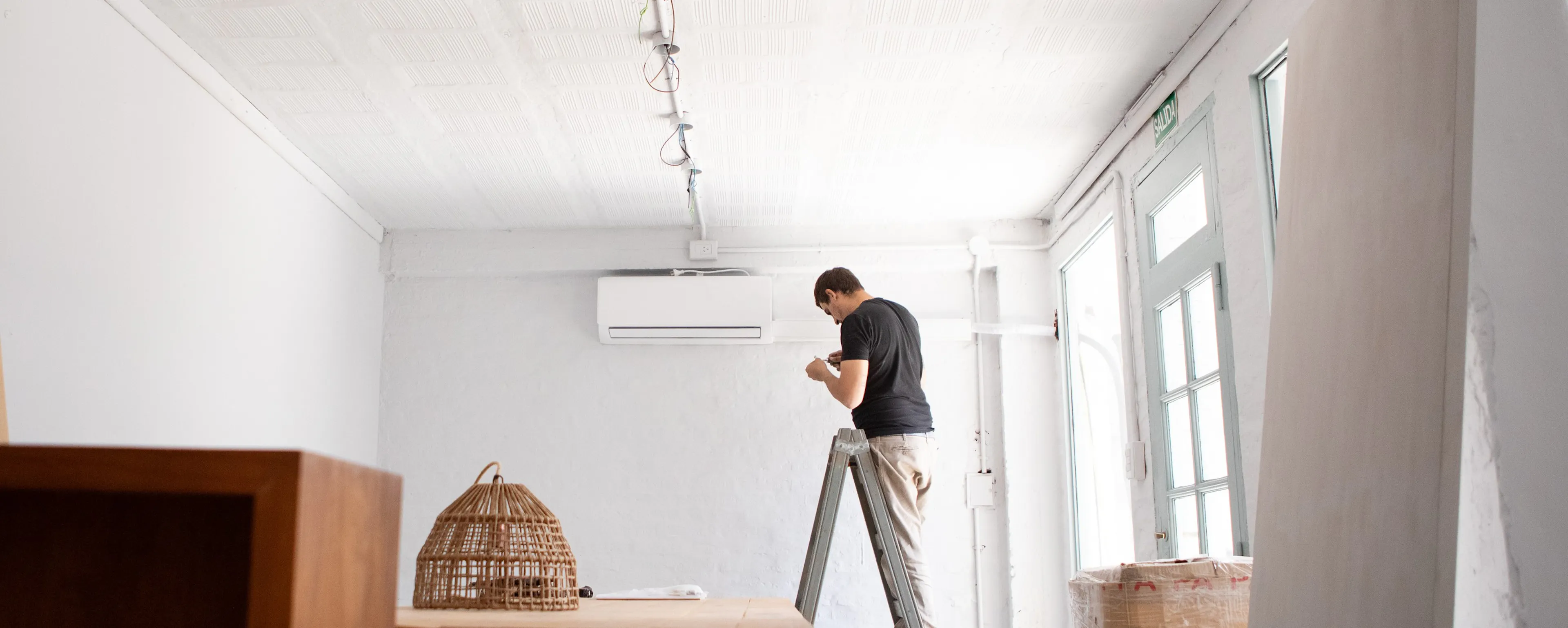Homme sur une échelle installant l'unité intérieure de sa climatisation. Installer soi-même sa clim : grosse erreur ou bonne idée ? 