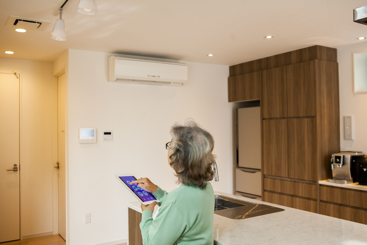 Une femme âgée pilote la climatisation de son salon via sa tablette