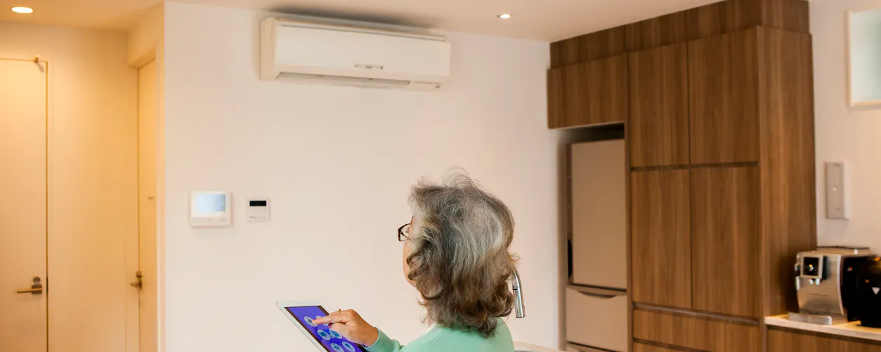 Une femme âgée pilote la climatisation de son salon via sa tablette
