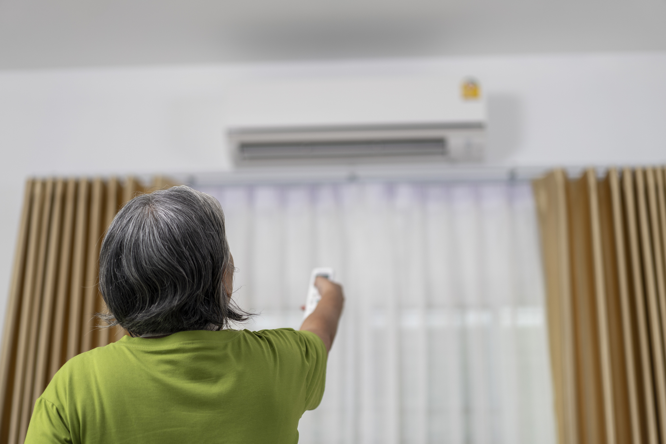 Une femme aux cheveux grisonnants règle la température de sa climatisation grâce à sa télécommande