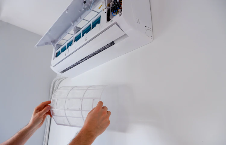 Une personne remet en place le filtre propre de son unité intérieure de climatisation