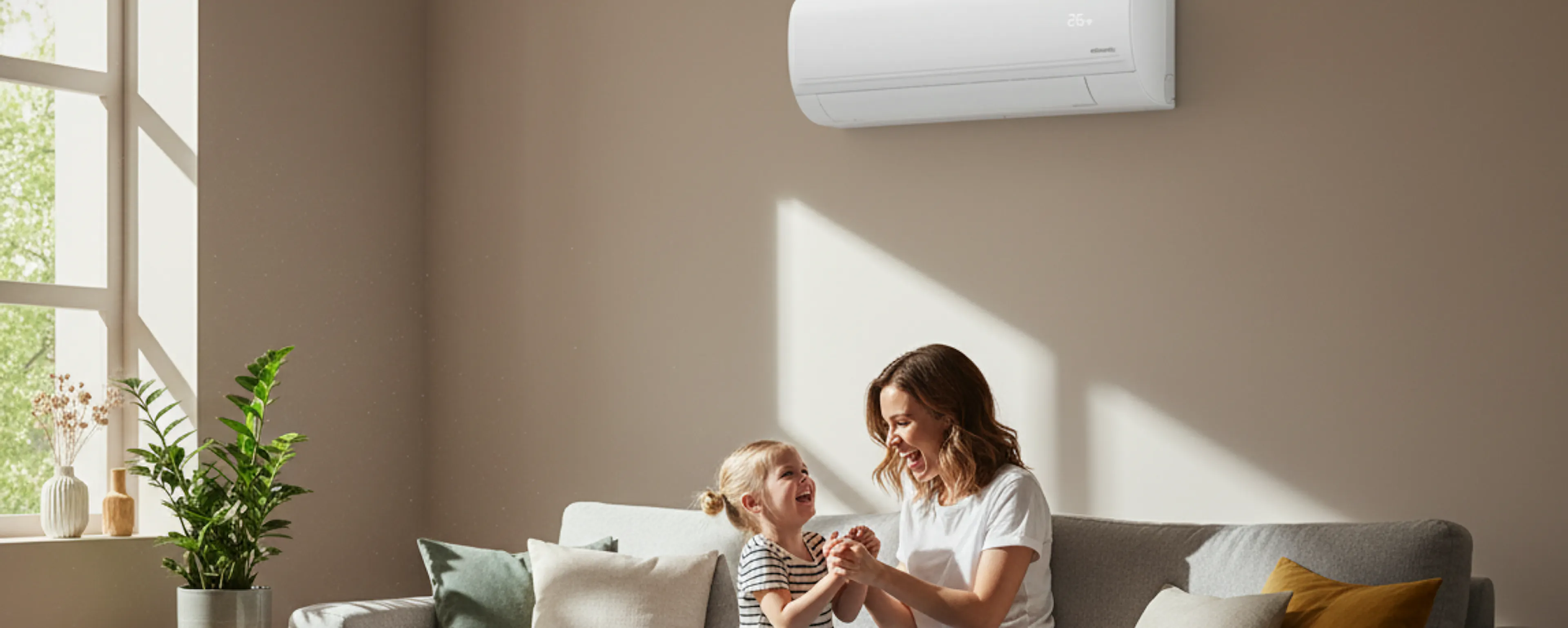 Une mère et sa fille jouent dans le salon lumineux de leur maison, sur le mur derrière elles, un climatiseur Atlantic Murao Smart blanc mat