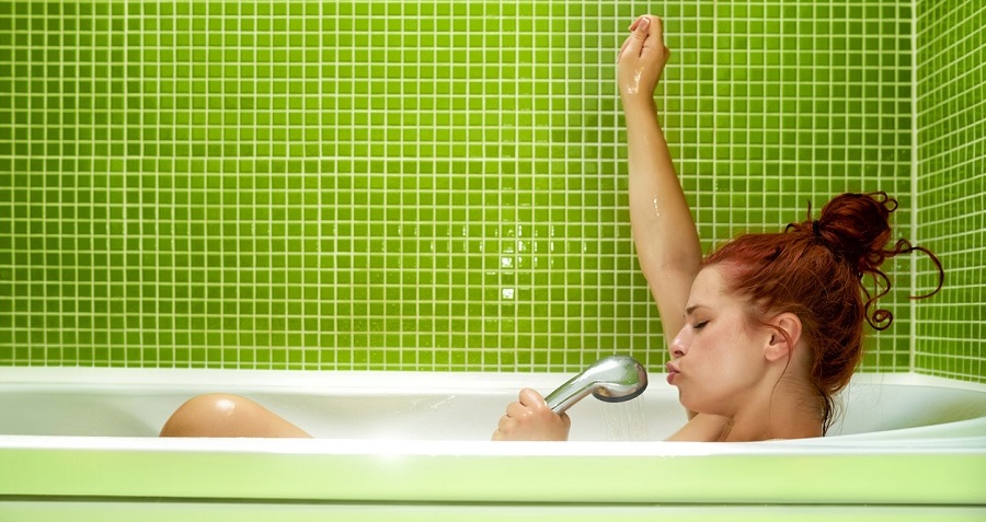 Femme se relaxant dans un bain avec pomme de douche sur carrelage vert