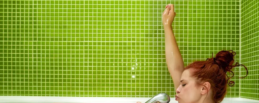 Femme se relaxant dans un bain avec pomme de douche sur carrelage vert