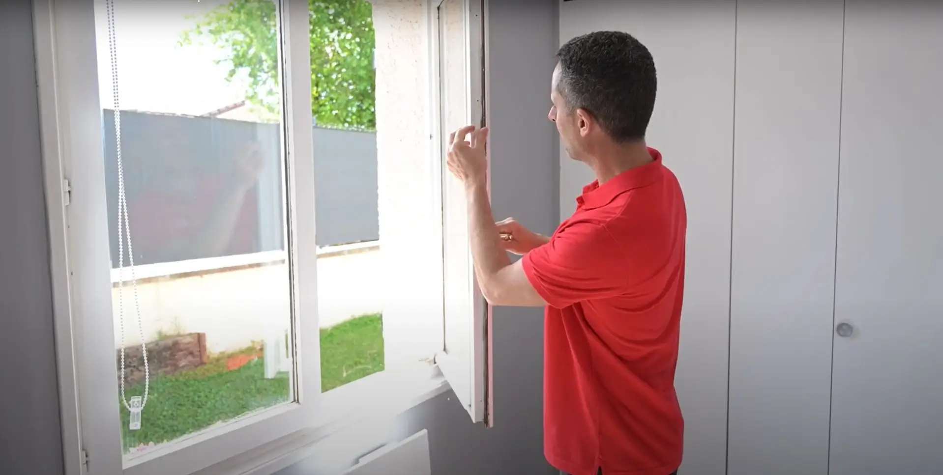 Homme en rouge inspectant le joint d'une fenêtre en PVC
